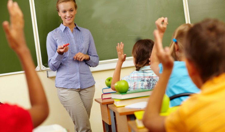 Portrait of smart teacher by blackboard looking at schoolkids in classroom