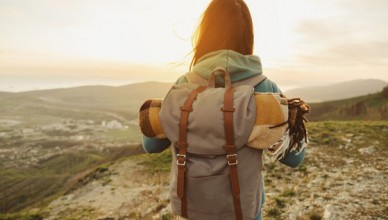 Hiker woman with backpack and sleeping bag walking in the mountains in summer at sunset
