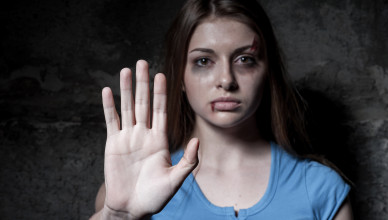 Stop hurting woman! Young beaten up woman looking at camera and stretching out hand while standing against dark wall