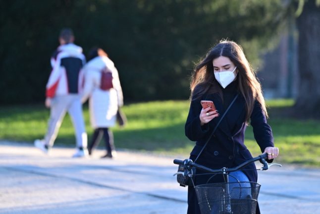 A women wearing a protective face mask rides her bike as she looks at her smartphone in the interior courtyard of the Sforza castle in the center of Milan on January 13, 2021. - Italy's health minister announced on January 13, 2021 a partial reopening of museums, while most other coronavirus restrictions were due to be extended, measures that would apply only to less-infected "yellow" regions, while "respecting all social distancing measures". Italy, which has recorded nearly 80,000 deaths from the pandemic, has had colour-coded regional virus restrictions since November, when all the museums were shut. (Photo by Miguel MEDINA / AFP)