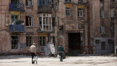 Local civilians walk amid destroyed buildings in Mariupol near the Illich Iron & Steel Works Metallurgical Plant in territory under the government of the Donetsk People's Republic, eastern Ukraine, Friday, May 27, 2022. (AP Photo/Alexei Alexandrov)