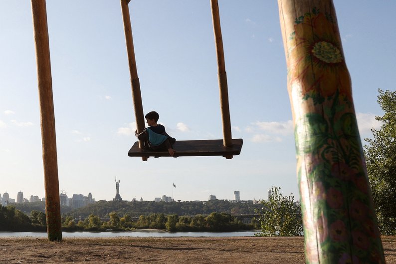 TOPSHOT - A boy rides on a wooden swing next to the Dnieper river with the Motherland Monument (L) in the background in the Ukrainian capital of Kyiv on October 3, 2023. (Photo by Anatolii STEPANOV / AFP) (Photo by ANATOLII STEPANOV/AFP via Getty Images)
