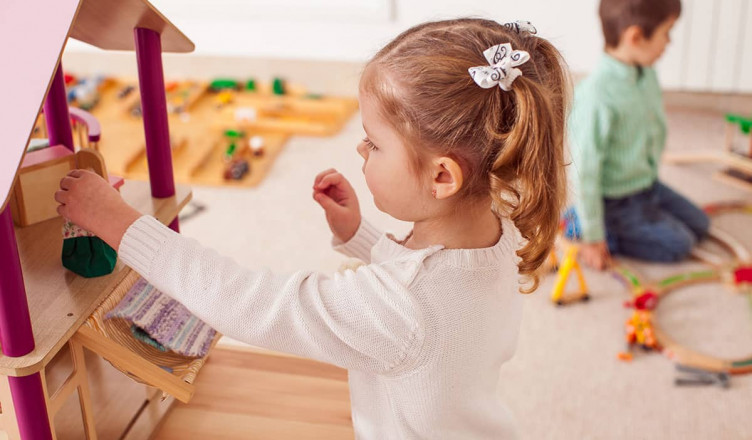 Beautiful little girl playing with a wooden dollhouse