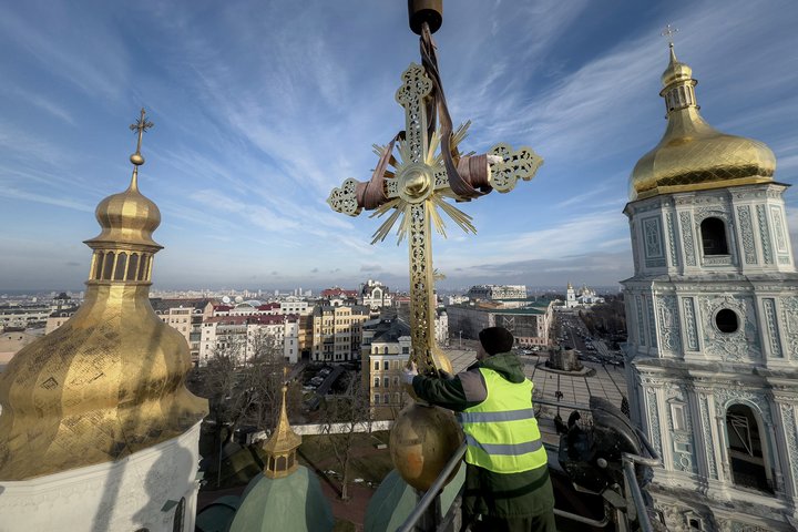 Ihor Kuzmenko, altitude worker installs a restored cross on a dome of Saint Sophia Cathedral in Kyiv, Ukraine, Thursday, Dec. 21, 2023. A UNESCO World Heritage site, the gold-domed St. Sophia Cathedral, located in the heart of Kyiv, was built in the 11th century and designed to rival the Hagia Sophia in Istanbul. The monument to Byzantine art contains the biggest collection of mosaics and frescoes from that period, and is surrounded by monastic buildings dating back to the 17th century. (AP Photo/Evgeniy Maloletka)