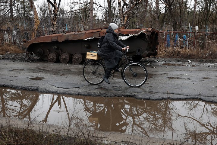 TOPSHOT - A woman rides a bicycle past a destroyed armoured military vehicle in the Svyatogirsk town, Donetsk region, on January 27, 2024, amid the Russian invasion of Ukraine. (Photo by Anatolii STEPANOV / AFP) (Photo by ANATOLII STEPANOV/AFP via Getty Images)