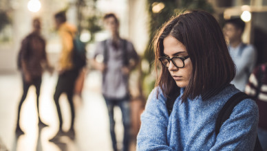 Displeased female student bullied by her classmate standing alone in a hallway.