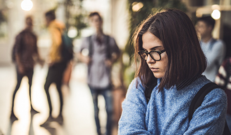 Displeased female student bullied by her classmate standing alone in a hallway.