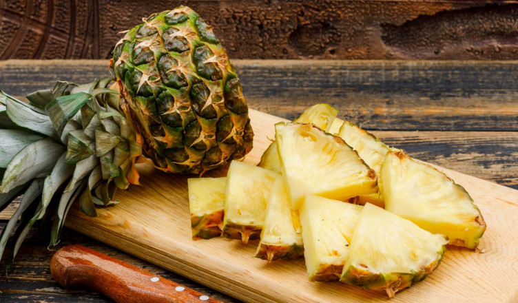 Sliced pineapple in a cutting board with a fruit knife side view on a wooden grunge and stone tile background