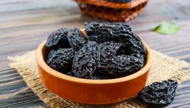Prunes in a clay bowl and fresh plums, leaves on a wooden table. Fresh prunes for healthy life.