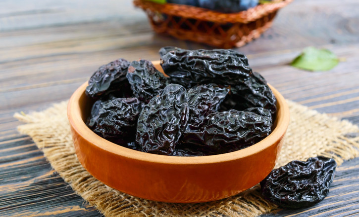 Prunes in a clay bowl and fresh plums, leaves on a wooden table. Fresh prunes for healthy life.
